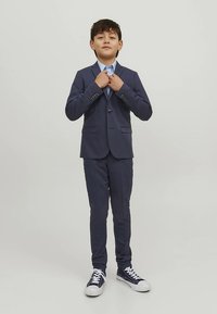 Tumesinine ülikond, millel on ühekohaline bleiser ja kitsad püksid, kombineeritud helesinise särgi ja vabaajajalatsitega.