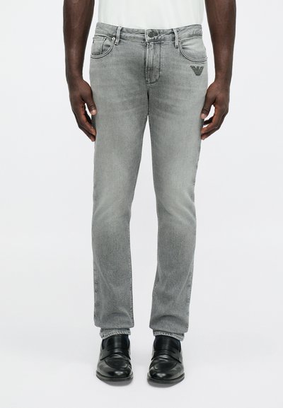 Γκρι τζιν παντελόνι με στενή εφαρμογή, διαθέτοντας πέντε τσέπες και ραμμένο λογότυπο στην πίσω τσέπη. Φοριέται με μαύρα παπούτσια.