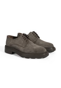 Une paire de chaussures de ville pour homme en cuir suédé marron, à lacets, avec des semelles en caoutchouc épaisses, sur fond blanc.