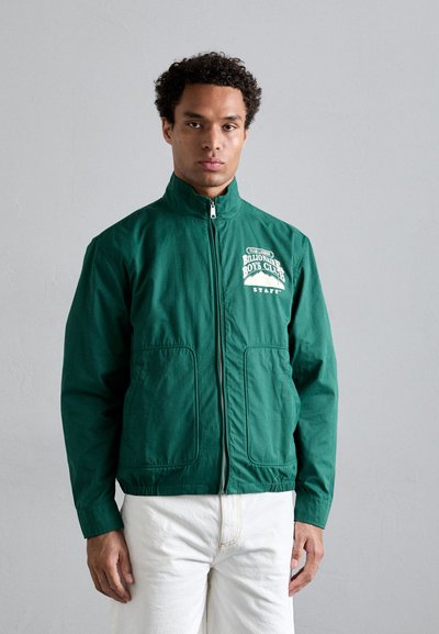 Grüne, leichte Jacke mit hohem Kragen, Frontreißverschluss, zwei seitlichen Taschen und weißem Logo-Druck auf der linken Brust. Glatte Textur.
