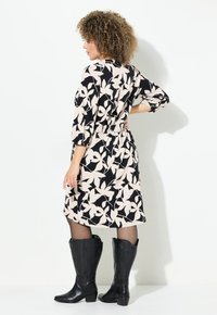 Blumenmusterkleid in Schwarz und Creme, tailliert mit einem gerafften Gummiband, kombiniert mit hohen schwarzen Stiefeln.