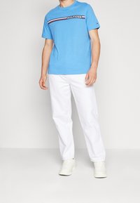 Ljusblå bomulls-T-shirt med en horisontell röd och marinblå rand, matchad med vita byxor och vita sneakers. Standard passform.