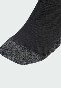 Calzino nero con una parte superiore testurizzata e una punta grigia a fantasia. Il materiale sembra lavorato a maglia, combinando design solidi e fantasie.