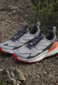 Szare buty sportowe z teksturowaną cholewką, pomarańczowymi akcentami, czarną podeszwą i amortyzującą podeszwą środkową. Posiadają sznurowany system zapinania i uchwyt do zakupu.