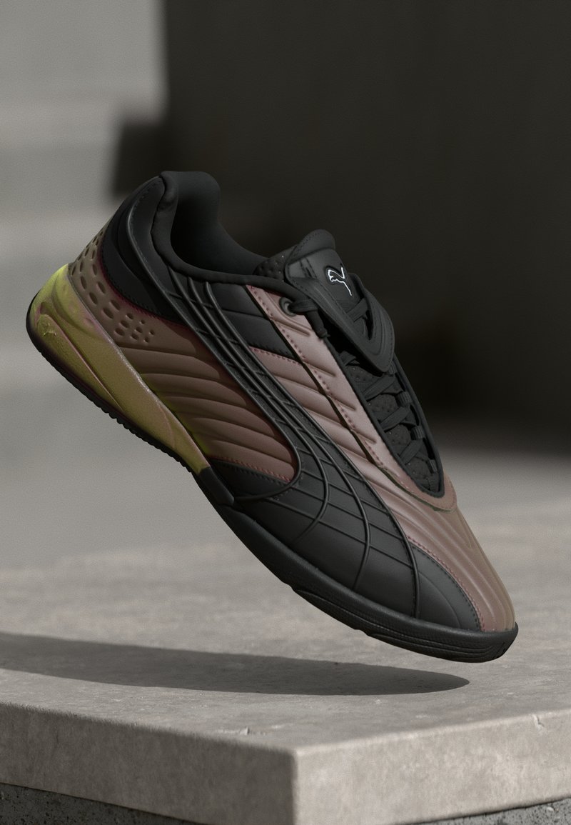 Sneaker Puma negru și maro cu talpă galbenă flotând deasupra unei margini de beton pe un fundal întunecat și neclar.