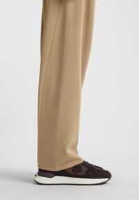Pantaloni beige, dal taglio morbido e con una texture liscia, abbinati a sneakers marrone scuro con una combinazione di scamosciato e rete, suola in gomma bianca.