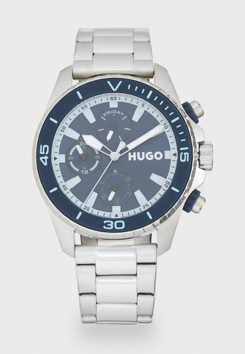 Chronograph watch with a silver stainless steel case, blue dial, and white bracelet. Features date, weekday, and sub-dials. Blue accents on bezel.