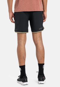 Sorte treningsshorts med en kontrasterende olivengrønn kant, laget av lett materiale og med en logo på det lavere beinet.