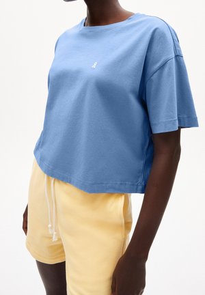 T-shirt en coton bleu court avec un col rond et des manches courtes, présentant un petit logo blanc sur la poitrine. Associé à un short jaune.