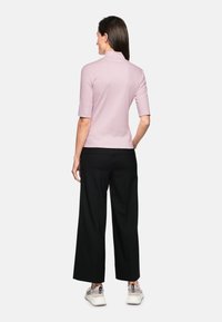 Pink short-sleeve top with a mock neck, paired with black wide-leg trousers and light sneakers. Smooth fabric and fitted design.