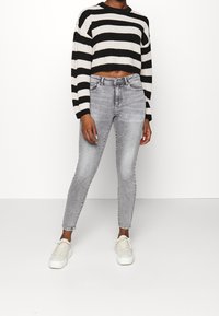 Suéter corto a rayas en blanco y negro, combinado con jeans skinny de talle alto en gris claro y zapatillas blancas. Texturas suaves en toda la prenda.