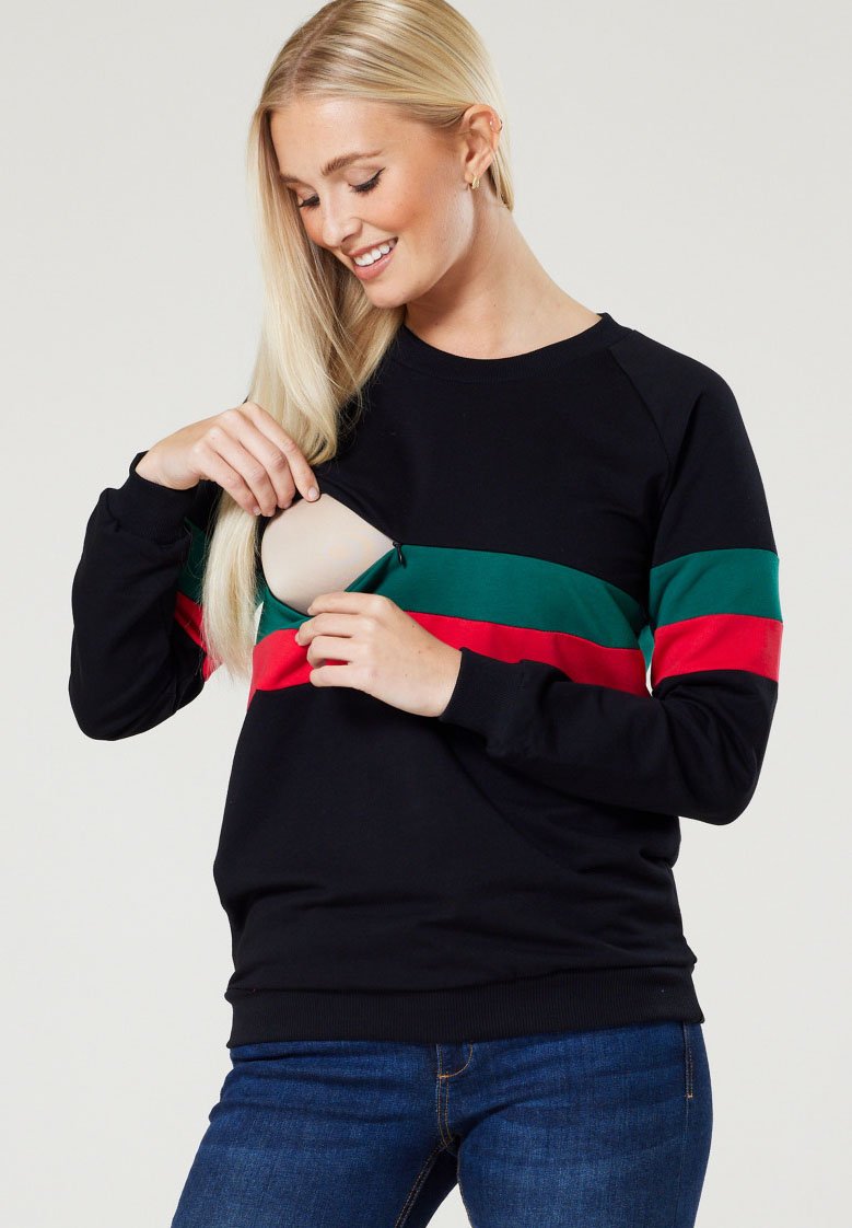 Črna trenirka z zelenimi in rdečimi vodoravnimi pr stripes. Ima stranski zadrgo za enostaven dostop, rebraste manšete in sproščen kroj.