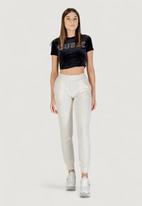 T-shirt cropped in velluto nero con logo "GUESS", abbinato a pantaloni tapered beige chiaro, con polsini elasticizzati e tasche laterali. Sneakers bianche.