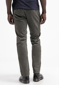Chinos verde oliva con taglio dritto, realizzati in tessuto leggero. Presentano tasche posteriori e dettagli di cucitura sottili. Abbinati a scarpe nere.