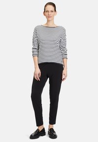 Schwarz-weißer, gestreifter Langarmoberteil mit weitem Ausschnitt, kombiniert mit schwarzen, schmal geschnittenen Hosen und glänzenden schwarzen Schuhen.