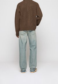 Brun stickad tröja, vida ljusblå denimjeans med fransade fållar och beige skor. Outfiten ses från ryggen.