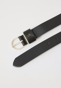 Ceinture en cuir noir avec une boucle rectangulaire dorée et une attache de marque. Texture lisse, coupe droite et plusieurs trous d'ajustement.