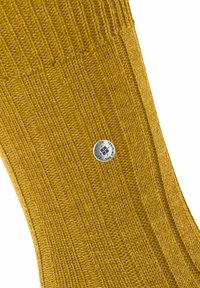 Calzino lavorato a maglia giallo senape con texture a coste e dettaglio circolare in argento. Tessuto liscio con schemi di cucitura a contrasto.