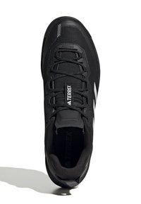 Czarne buty outdoorowe z siateczkowym wierzchem, wzmocnionym czubkiem, sznurowaniem i białym logo marki z boku. Teksturowana gumowa podeszwa.