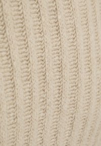 Crèmekleurige gebreide stof met verticale geribde texturen, die een zachte, garzige uitstraling vertoont met duidelijke, gestructureerde patronen.