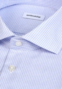 Chemise habillée bleu clair à carreaux avec col à boutons, boutons blancs et étiquette « seidensticker » près du col.