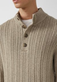 Beżowy sweter z prążkowanego dzianiny z wysokim kołnierzem, trzema guzikami i teksturowanym wykończeniem. Charakteryzuje się luźnym krojem oraz delikatnymi detalami w stębnowaniu.