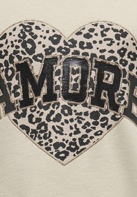 Sweat-shirt beige clair avec un grand cœur en imprimé léopard noir et le texte en gras "AMORE", souligné de paillettes dorées.