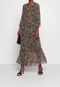 Robe maxi fleurie avec col en V, manches trois-quarts et ourlet à volants. Elle présente une base noire ornée de motifs floraux violets et jaunes.