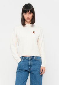 Pulover din tricot ribbed în nuanța crem deschis, cu guler înalt și mâneci lungi. Are un detaliu mic, brodat, cu un ursuleț pe piept.