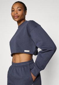 Marineblå, kort sweatshirt med lange ermer, med et rått nederste og en liten logoetikett. Jevn tekstur og avslappet passform, sammen med matchende joggebukser.