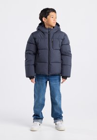 Merihenkinen puff takki, jossa on huppu, vetoketjukiinnitys, tikattu muotoilu ja rintatasku. Yhdistetty sinisiin farkkuihin ja valkoisiin nilkkureihin.