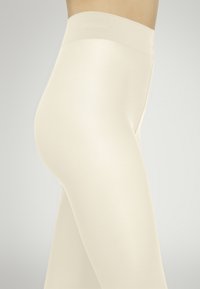 Leggings beige elasticizzati con una texture liscia e una cintura ampia e senza cuciture, progettati per comfort e facilità di movimento.