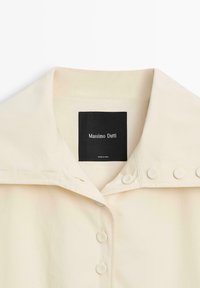 Crèmekleurige overhemdkraag met knopen aan de voorkant en een zwart Massimo Dutti merklabel aan de binnenkant van de halslijn.