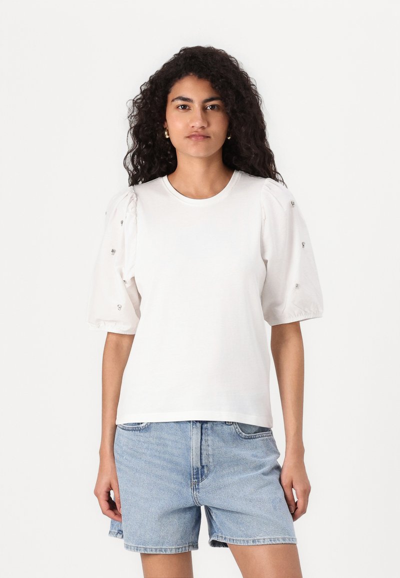 Vit bomull t-shirt med puffade kortärmar med små utsmyckningar, tillsammans med ljusblå denimshorts.