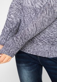 Maglione a maglia grigio scuro con macchie bianche. Presenta un orlo e polsini a coste, con una vestibilità ampia e un motivo testurizzato su tutta la superficie.