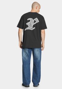 Czarny bawełniany t-shirt z dużą białą grafiką na plecach. W połączeniu z wyblakłymi niebieskimi spodniami o szerokich nogawkach. Projekt jest casualowy i luźny.