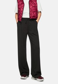 Black wide-leg pants with a drawstring waist, paired with a maroon quilted vest and white t-shirt, worn with patterned sneakers.
