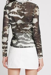 Genomskinlig långärmad topp i ett brunt och vitt abstrakt mönster, i kombination med en vit denim minikjol med två bakfickor.