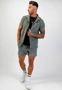 Ljusgrå kortärmad skjorta och matchande shorts, tillverkade i mjukt tyg. Svart t-shirt under, vita sneakers och randiga strumpor.