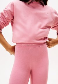 Felpa in cotone rosa chiaro con polsini a coste e un piccolo logo. Leggings rosa chiaro coordinati con una vita con marchio e una texture liscia.