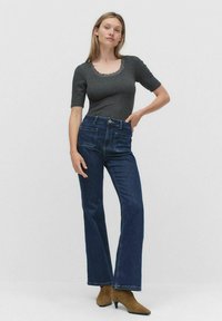 Mørkegrå tætsiddende top med scallop-halsudskæring, parret med lige ben mørkeblå jeans og brune ankelstøvler. Glat stof og klassisk design.