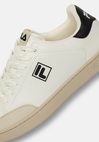 Vita skinnsneakers med svart hälaccent, rund tå, texturerad beige gummisula och framträdande svart logotyp på sidan. Snörningsdesign.