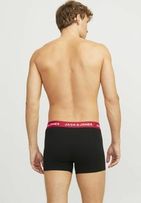 Bóxers negros con una cinturilla roja que presenta el logotipo "JACK & JONES". La tela parece suave y ajustada, sin patrones visibles.