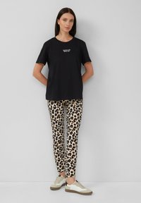 Schwarzes Baumwoll-T-Shirt mit weißem Text, kombiniert mit beigen Leggings im Leopardenmuster. Die Schuhe haben ein Design in Creme und Grau.