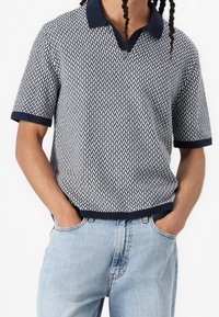 Polo de manga corta en patrón de zigzag en azul marino y blanco, con cuello y puños en azul marino liso. Fabricado en material de punto ligero, corte relajado.