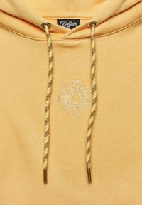 Gelbe Kapuzenjacke aus strukturiertem Stoff, mit einem Sonnen-Graphic und gestickten Details. Die Zugbänder sind mit braunen und gelben Akzenten geflochten.