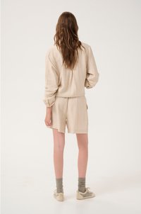 Beige korte set gemaakt van gestructureerde stof, met een losse top en shorts met subtiele patronen. Gecombineerd met grijze sokken en lichte schoenen.