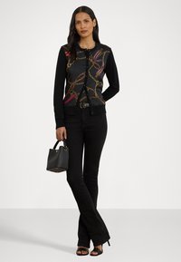 Μαύρο ζακέτα με διακοσμητική αλυσίδα και σχέδιο κορδέλας, συνδυασμένο με μαύρα τζιν ψηλόμεσα και μικρή μαύρη τσάντα. Σχεδίαση με ανοιχτό μπροστά.