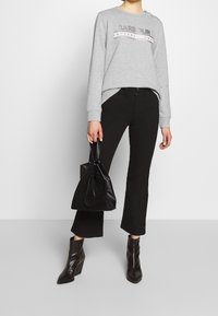 Grey sweatshirt with a round neckline, featuring a logo design. Black flared pants, shiny black ankle boots, and a black bag.
