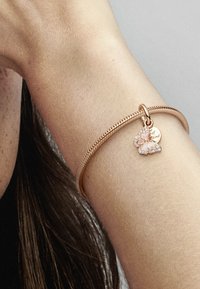 Bracciale in oro rosa con un design texturizzato e un charm a forma di farfalla adornato con accenti rosa e pietre trasparenti, con un ciondolo a forma di cuore.